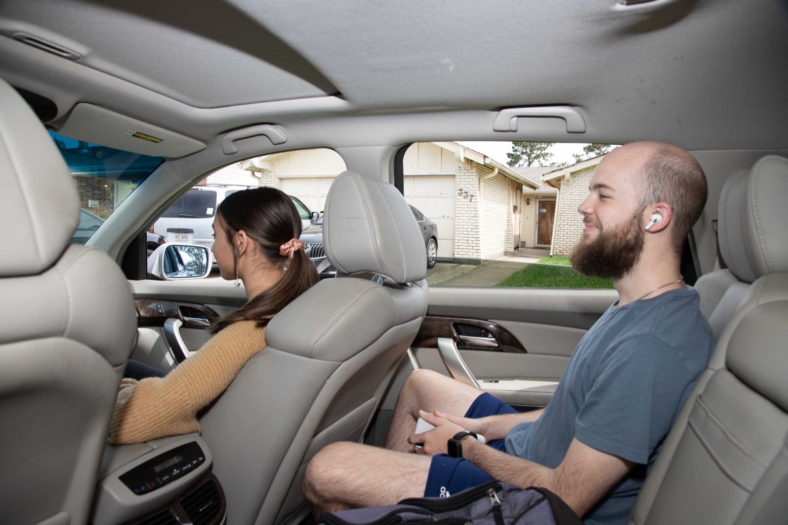 Two riders in the back seat of an SUV — one wearing earbuds — heading east on a Louisiana road