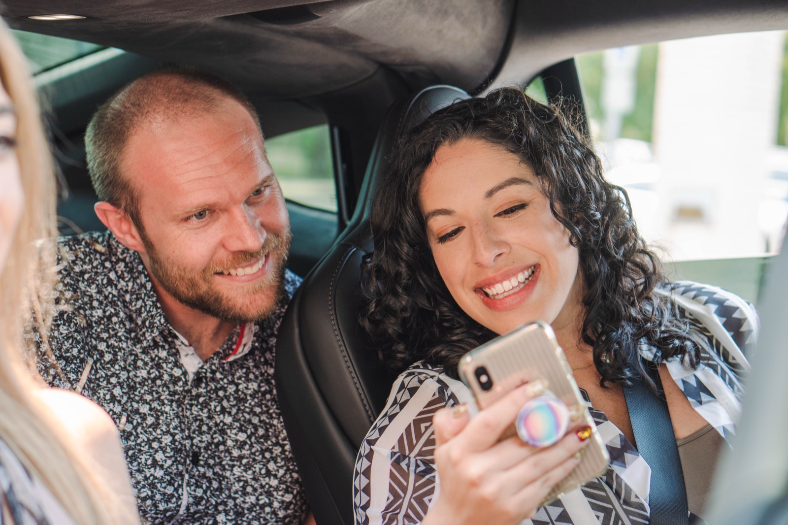 Three commuters in a car sharing a phone screen mid-ride, the GoCarma app visible